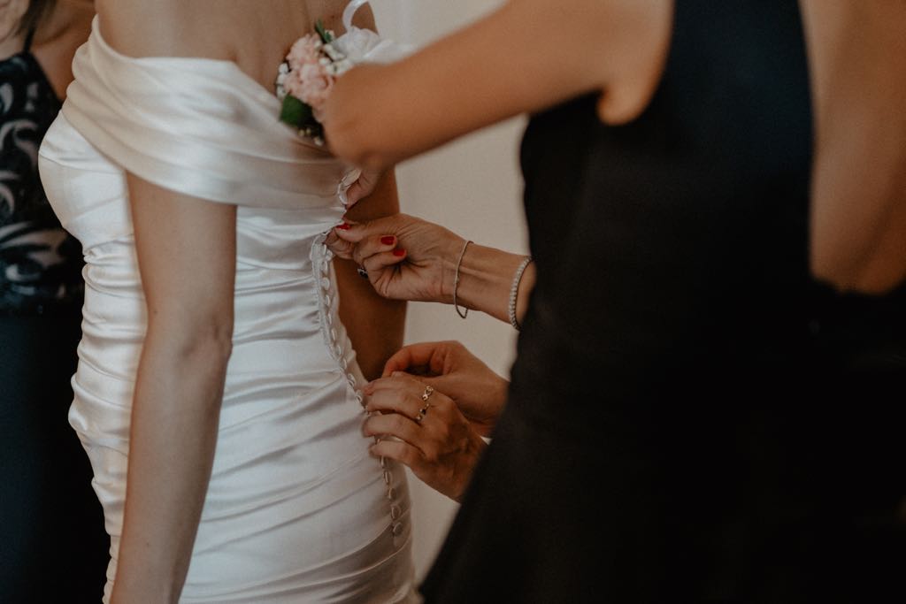 Un dettaglio delle mani della testimone durante la vestizione della sposa nel giorno del Matrimonio al Castello San Basilio