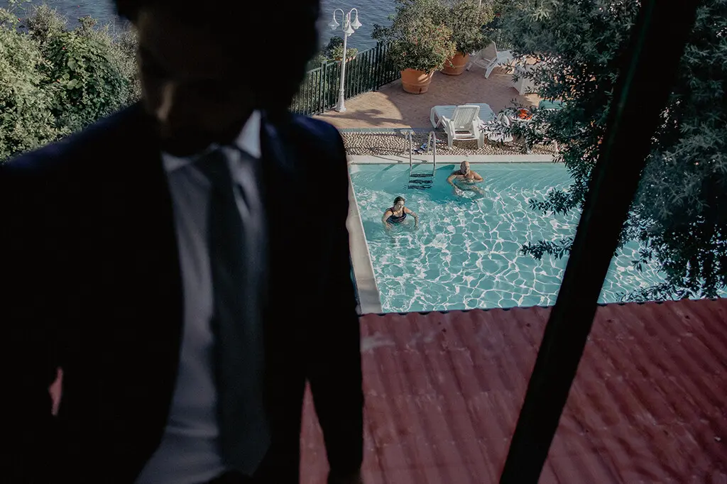 Ritratto dello sposo, sullo sfondo due persone che fanno il bagno in piscina, Hotel Villa del Mare a Maratea, Giuseppe Bruno wedding reportage in Basilicata